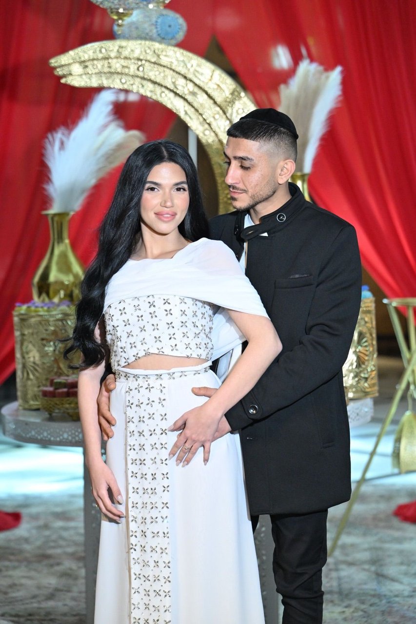 זוג חתן וכלה על רקע תפאורת סהר מוזהב ווילונות אדומים